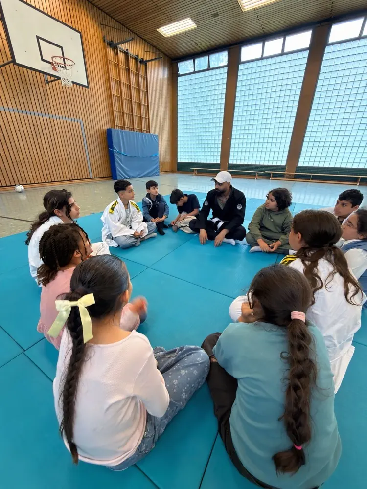 Kinder sitzen im Kreis auf der Trainingsmatte beim Kinzoku Brazilian-Jiu-Jitsu-Training